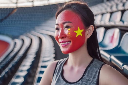 Happy smiling Asian woman, fan of the Chinese team in the stands of the sports stadium during the Olympics with the Chinese flag painted on her face