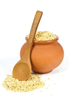 Manna croup in a clay pot with a wooden spoon on a white background
