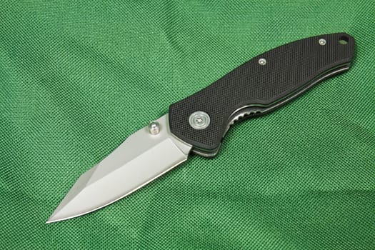 Folding knife with a black handle and lock on green canvas