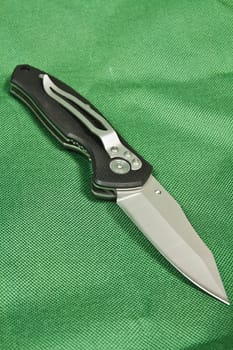 Folding knife with a black handle and lock on green canvas