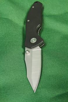 Folding knife with a black handle and lock on green canvas
