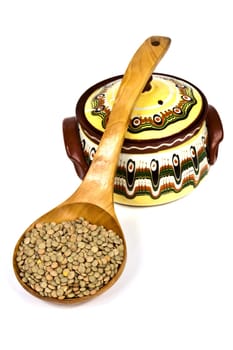 Wooden spoon full of raw lentils supported a color ceramic pot