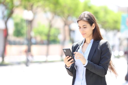 Young executive checking cell phone walking in the street