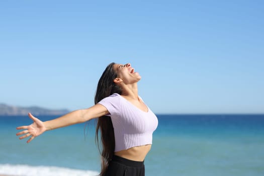 Happy woman screaming outstretching arms on the beach