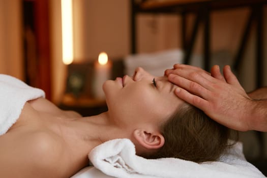 Spa salon, appointment at chiropractor. Side view tranquil female patient sleeping under therapist hands on forehead