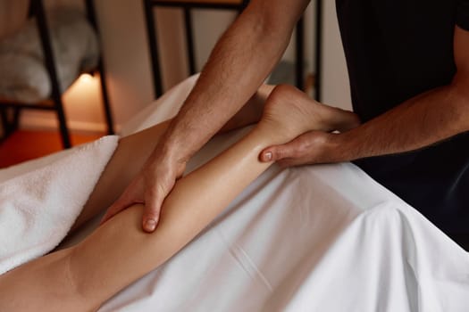 Crop of therapist massaging female leg in spa salon healing cramp muscle pain. Cosmetology and body treatment procedure