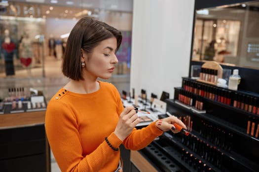 Woman in cosmetics shop testing lipsticks on her hand. Lady customer choosing suitable pomade in shopping mall