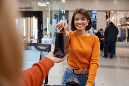 Attractive positive lady working in cosmetics store making a purchase. Smiling saleswoman in shop with stuff for face