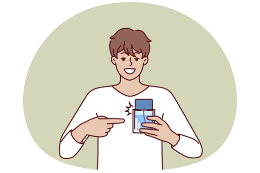 Man pointing finger at perfume bottle recommending to buy cologne or antiperspirant with cool scent. Happy guy employee of perfume shop holding sample of deodorant that protects against bad smell