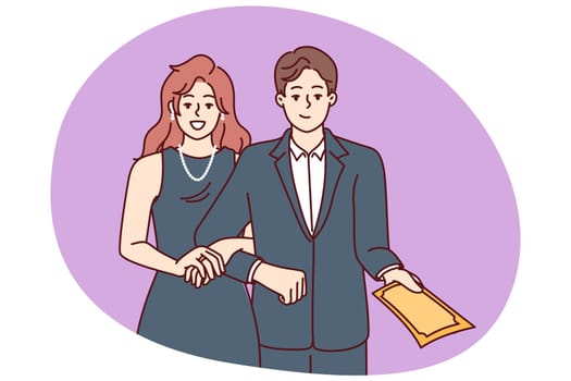 Elegant man and woman in formal evening wear for event holding hands demonstrating invitation to ceremony. Family couple in tuxedo and dress for attending theater or awards ceremony for celebrity