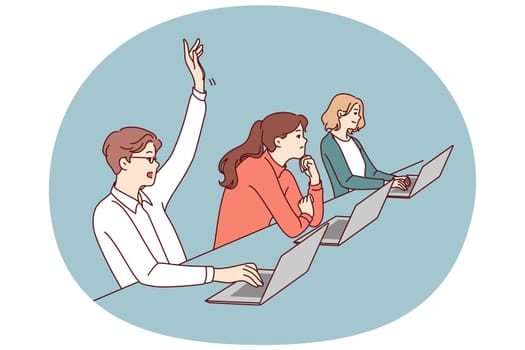 Man student sitting at desk with laptop raises hand to attract attention of teacher and ask question on topic of lecture. People listening to lecture in college or university auditorium