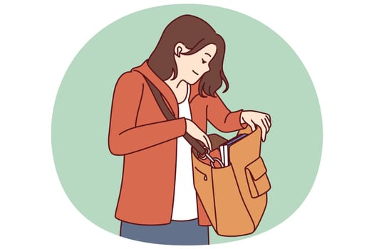 Woman looks into large bag hanging on shoulder in search of wallet or phone lost in handbag. Tourist girl with handbag dressed in casual clothes is trying to find lost or stolen personal items.