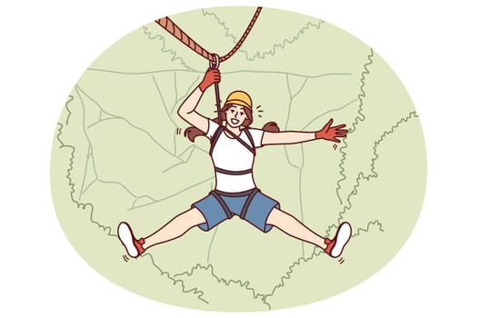 Woman tourist hangs on zip line over forest cliff enjoying extreme vacation in picturesque place. Tourist girl descends from mountain on rope getting adrenaline from adventures while traveling
