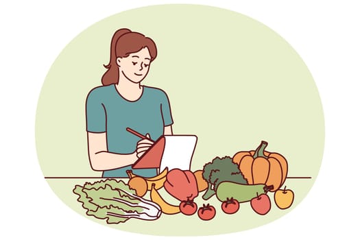 Woman nutritionist is standing near table with vegetables and making notes in notebook, making plan for new diet to detoxify body. Girl nutrition specialist uses checklist to mark diet ingredients