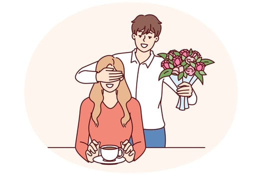 Romantic man with bouquet closes girlfriend eyes, wanting to make surprise and give favorite flowers. Romantic groom came on date with flowers for bride drinking coffee in cafe or bar
