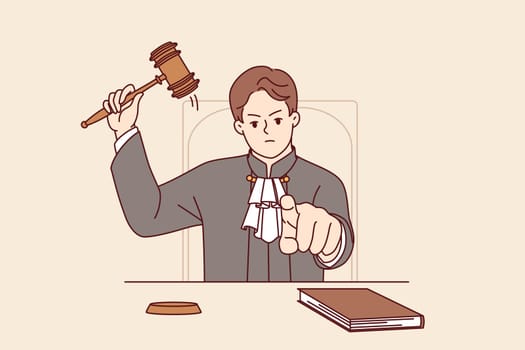 Stern judge pronounces verdict and points finger at screen after hitting gavel and announcing prison term. Angry judge sits at table demonstrating inflexibility and desire to punish criminal