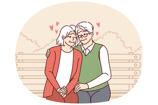 Elderly couple in love sits on park bench hugging and enjoying happy family life. Relationship between elderly man and woman in love sitting hugging and having fun from retirement.