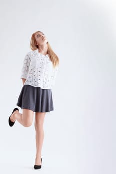 Confident young woman stands on one leg, hands behind back, looking up with a curious expression on a white background