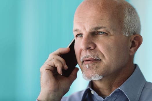 Mature businessman with a serious expression is holding a smartphone to his ear, listening intently to the conversation