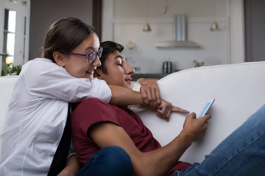 young woman, wearing glasses and a white shirt, points at the young mans smartphone. He appears amused, suggesting they are sharing a funny or interesting moment together