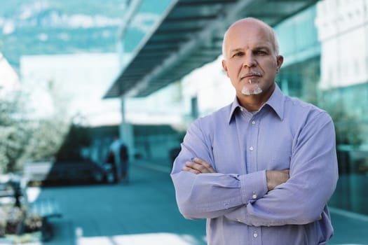 Portrait of a confident senior businessman standing with arms crossed in a modern office building, embodying experience and success in the corporate world