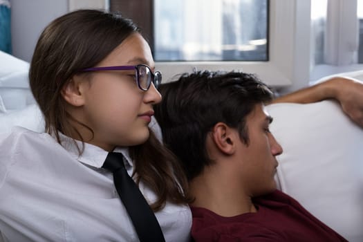teenage couple sits close together, both appearing concerned. The girl looks pensive, while the boy leans on her shoulder, reflecting a moment of relationship crisis or jealousy
