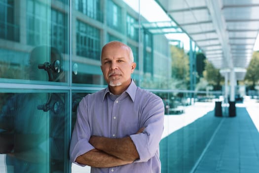 Confident mature businessman in modern office building, arms crossed, exuding experience and determination