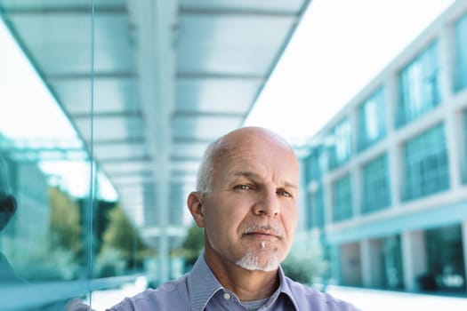 Mature businessman with a goatee standing outside a modern office building, thinking about the future and business strategies. His serious expression shows ambition and determination