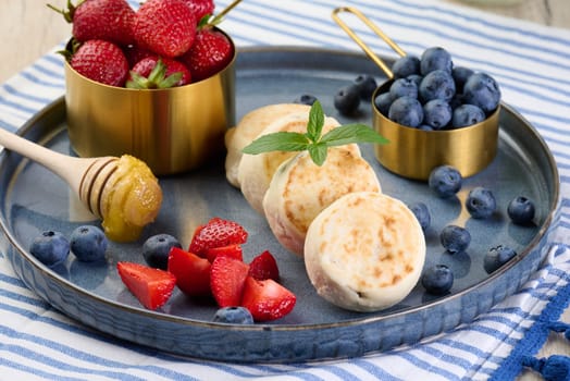 Round small fried cheesecakes on a blue plate with berries. Healthy breakfast