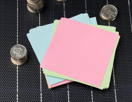 A stack of coins and paper stickers stands on a solar panel, budget savings when using renewable electricity