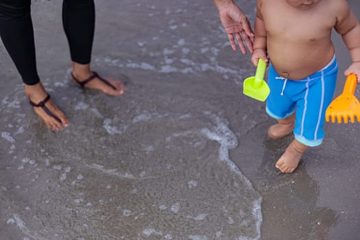 Little boy in blue shorts playing sand in the beach with his mother.