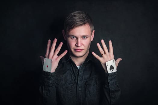 Confident tricky gambler with aces up sleeves. Illusionist showing tricks with playing cards isolated on dark background. Gambling games, luck and delusion concept