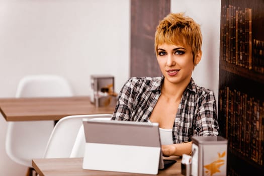 Confident young woman with short blonde hair works on a laptop in a cozy cafe, embodying modern digital nomad lifestyle
