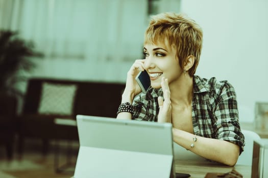 Freelancer is working from home, talking on her smartphone and gesturing with her other hand while looking away from her laptop