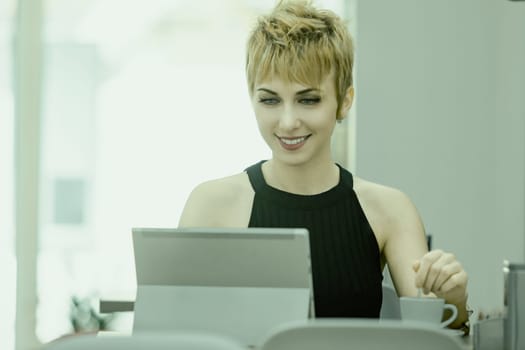 Smiling young woman with short blonde hair works on her laptop in a bright office, exuding confidence and determination