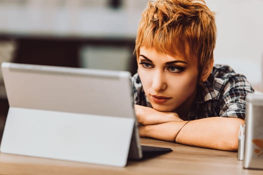 Young woman leaning on a desk in her home office, looking at a tablet screen with a serious expression, focusing on analyzing content