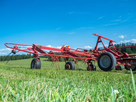 Ground level wide angle view of a red hay tedder on a pasture in the Bavarian Allgäu in summer.