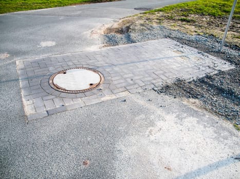 Newly constructed shaft with manhole cover on a rural asphalt road in bavaria.