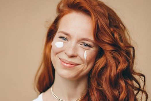 Close-up face of happy redhead smiling young woman with cream smears on cheeks.