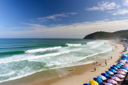 Aerial view of people on the beach, with colorful blankets and umbrellas.