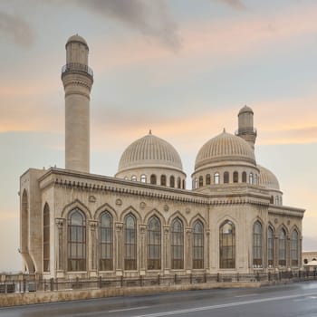 Bibi-Heybat Mosque in Baku, Azerbaijan, with its iconic minaret, domes, and intricate facade, glows in the sunset. Picture-perfect scene