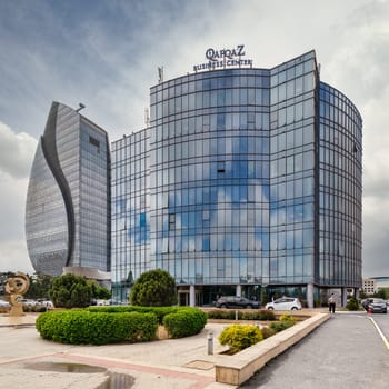 Baku, Azerbaijan - May 7, 2024: Qafqaz Business Center, a modern glass building against a backdrop of skyscrapers and a blue sky with white clouds