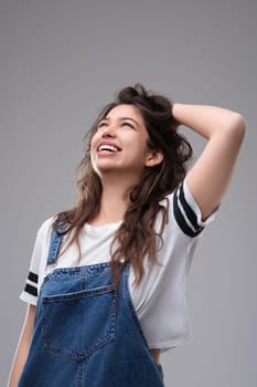 Young woman with long brown hair smiles happily in a studio shot, radiating joy and positivity while touching her hair, embodying carefree beauty and optimism