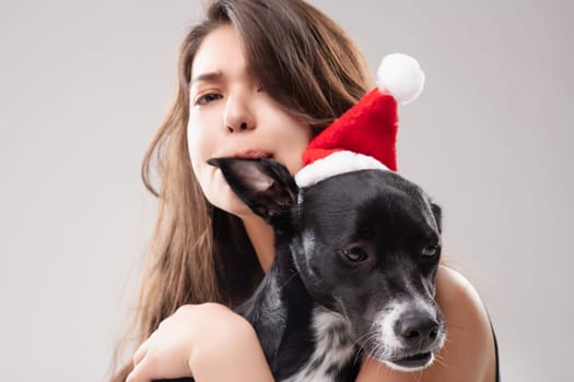 Woman hugs her dog in santa hats, radiating joy and love during the festive season