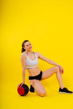 Portrait of a fitness happy fit woman standing holding a medicine ball. Copy Free space for text. Slim caucasian cross fit woman with fitness ball stand in gym, look. Plain light wall background