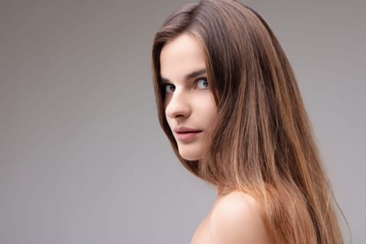 Beautiful young woman with long brown hair poses elegantly in a studio, exuding natural beauty and glamour. Perfect for beauty and fashion projects