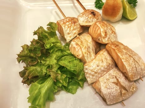 Grilled salmon belly on skewers on a white plate.