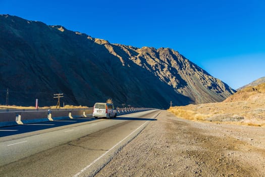 Car is driving along the road through natural mountain landscape with concrete barrier at sunny autumn day in Boom Gorge, Kyrgyzstan - December 16, 2022
