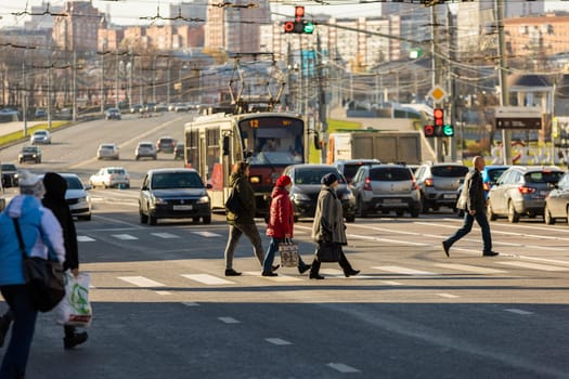 pedestrians crossing road in front of cityscape at sunny morning in Tula, Russia - October 23, 2021