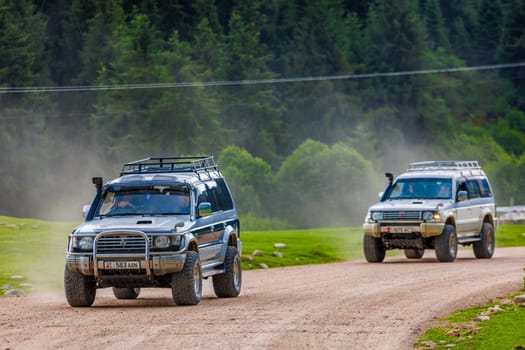 Two SUVs on rugged forest road, leaving dusty paths, symbolizing adventure and exploration in nature in Semenovskoye gorge, Kyrgyzstan at July 5, 2023